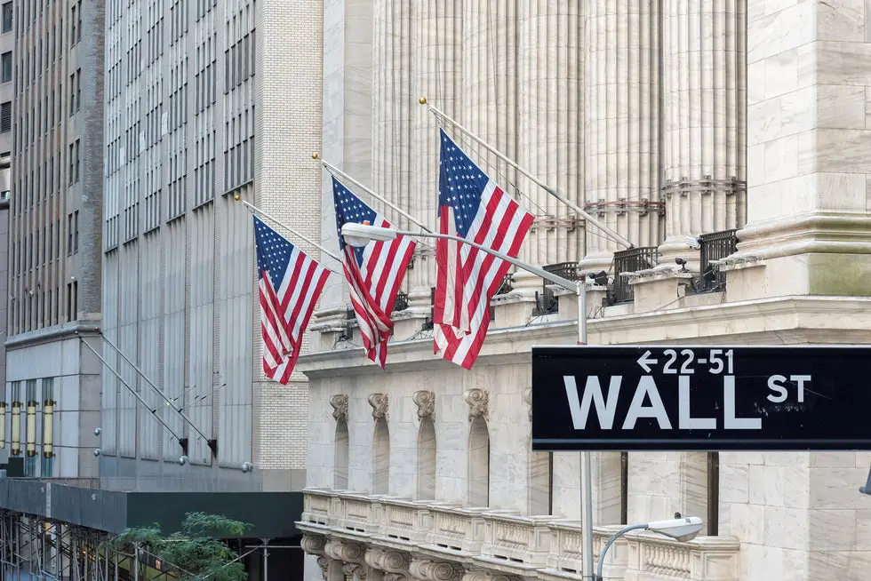 Three american flags hanging on a building in front of the wall street sign.